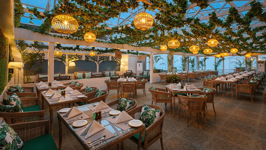 A covered terrace restaurant displaying set tables beneath hanging ceiling foliage and lights at Ramada by Wyndham Mussoorie Mall Road.