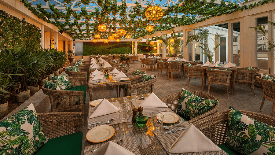 An outdoor dining space featuring tables, woven chairs, and hanging leafy decor overhead at Ramada by Wyndham Mussoorie Mall Road.