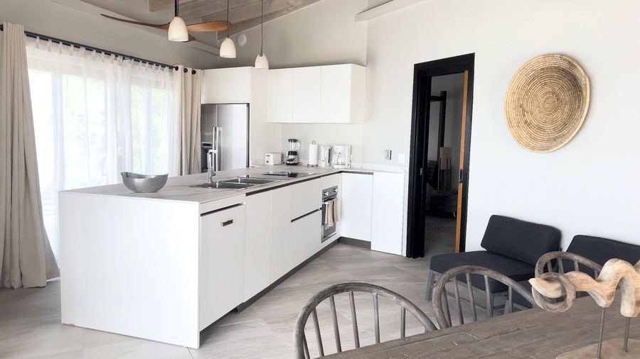 A kitchen area with an island with a sink, two lounge chairs, a table and two chairs at Tamarind Hills Resort and Villas, Antigua.