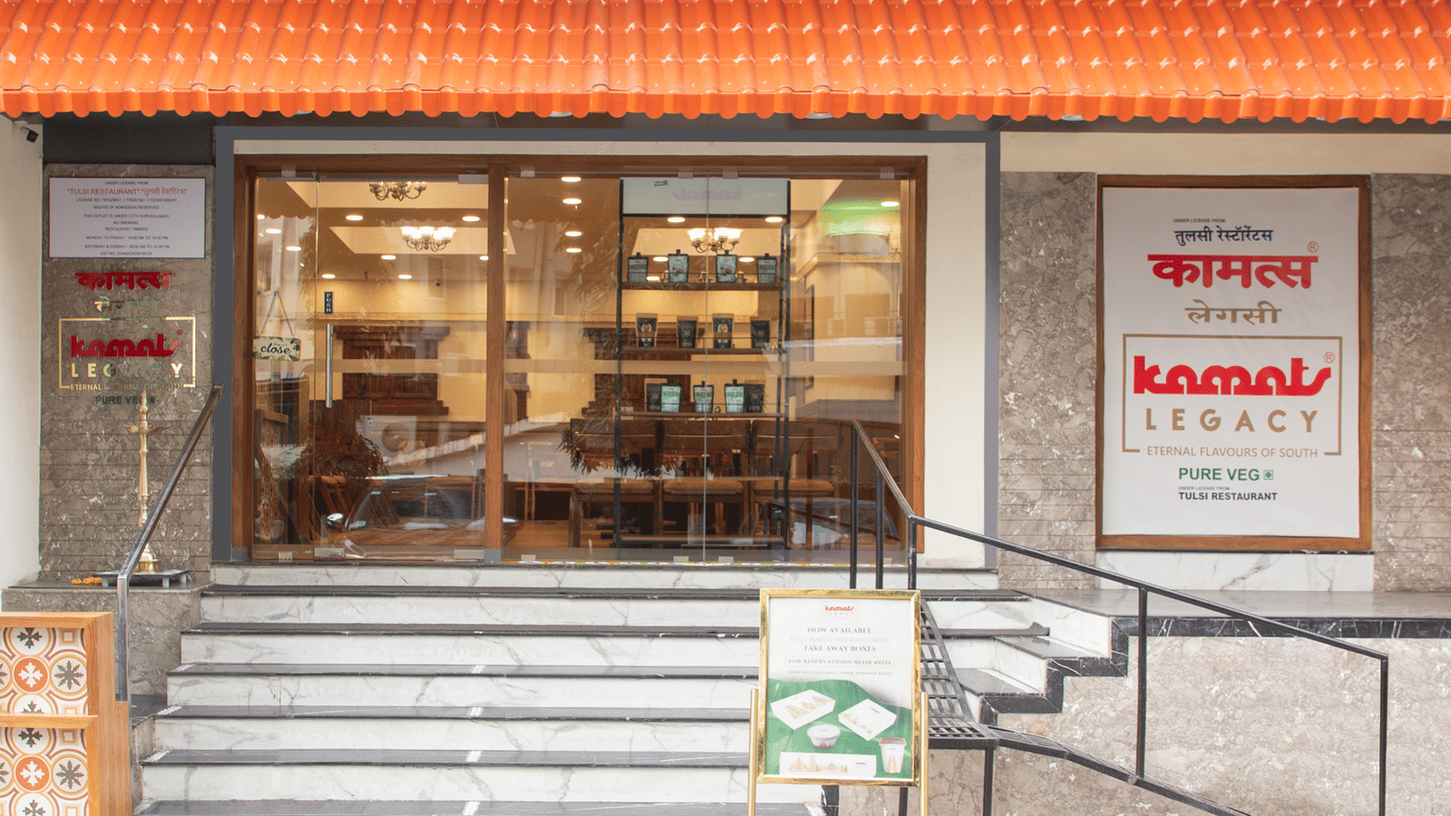 Front view of Kamats Legacy Nariman Point with steps leading to a modern glass entrance, combining urban style with classic branding.