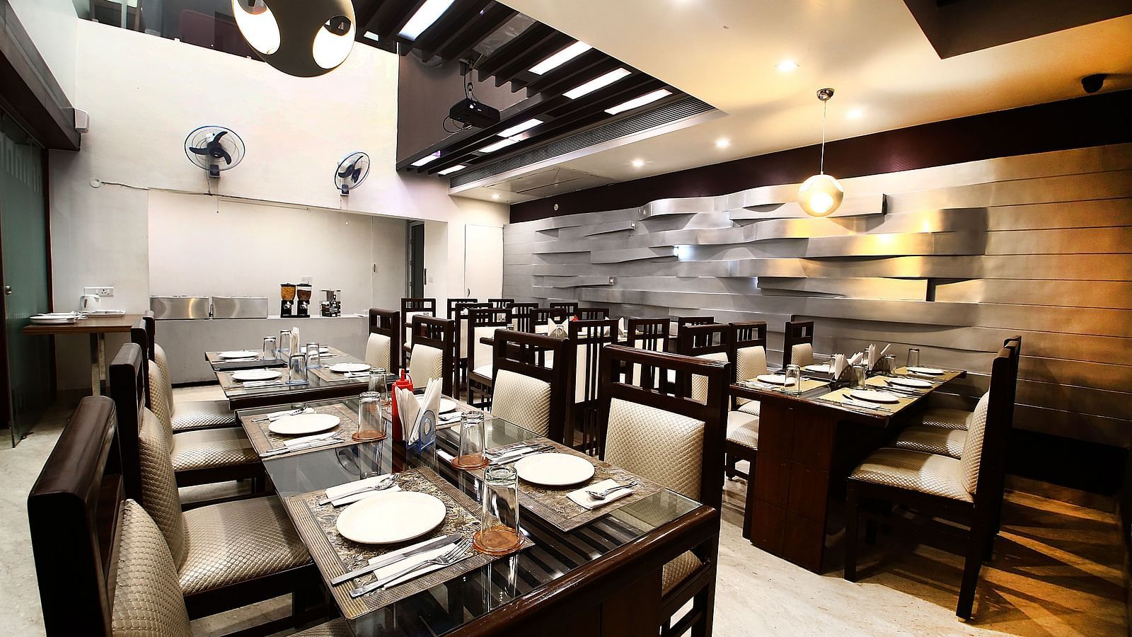 An elegant restaurant dining area with neatly arranged tables, chairs, place settings, and decorative lighting - Diamond Hotels