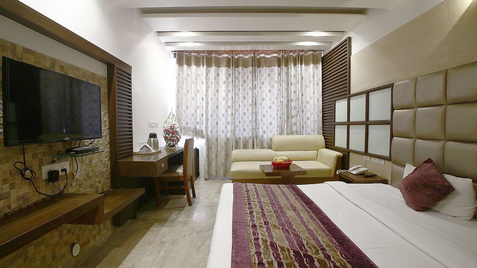 A well-designed hotel room with a large bed, wall-mounted television, and a neatly arranged workspace - Hotel Emerald, Chandigarh