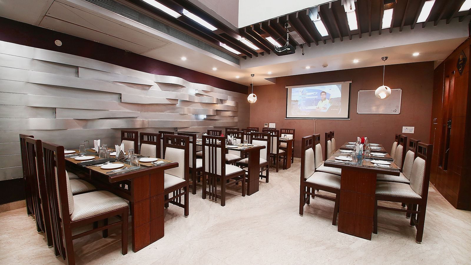 Modern dining space with various tables and chairs for guests to sit in and dine along with beautiful textured patterns on the wall and ambient  lighting - Hotel Emerald, Chandigarh