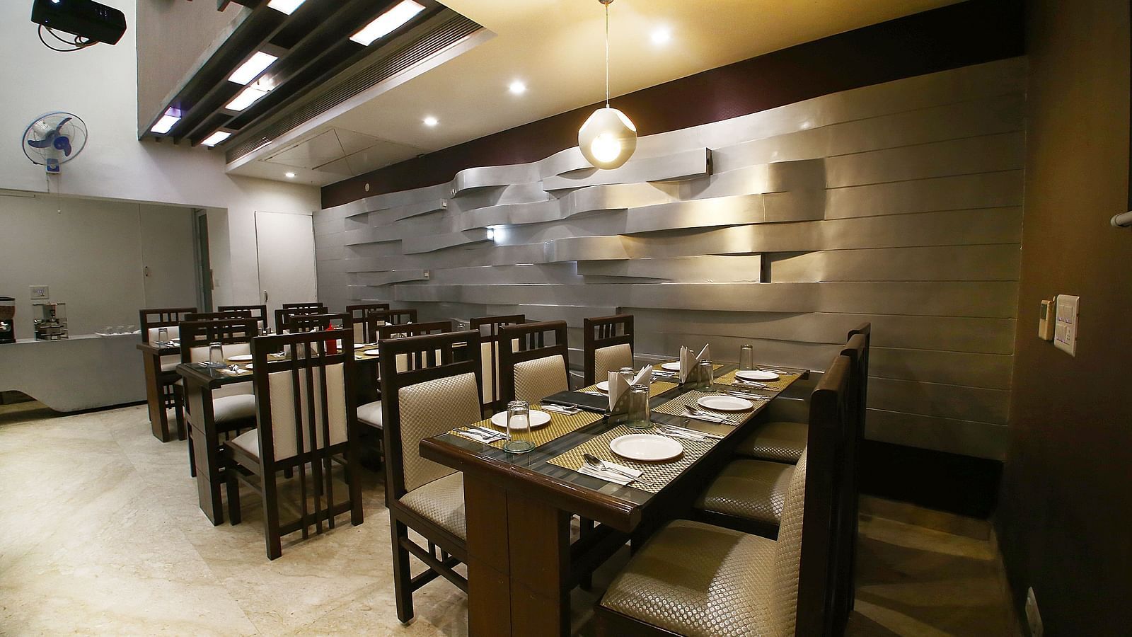 Uniformly placed chairs and tables of mocha and dark shades  in a modern light setting an extremely detailed walls and interior - Hotel Emerald, Chandigarh