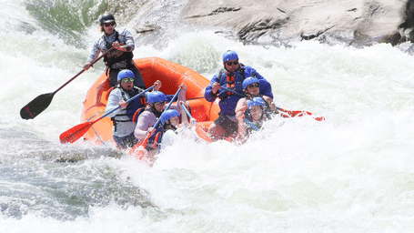 A group of tourists wearing life vests engaging into a rigorous river current on a raft.