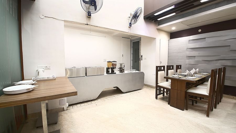 Dining space with a table and four chairs around it in a corner, a table with white plates and a desk with utensils along with two fans in a modern interior setting - Hotel Emerald, Chandigarh