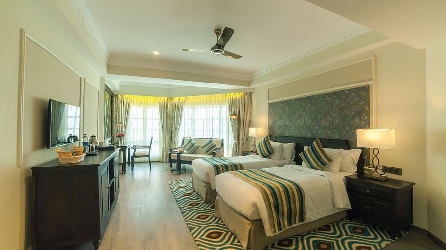 Spacious bed with furniture for seating, a bedside table, and a wall-mounted television at Fragrant Nature Cochin