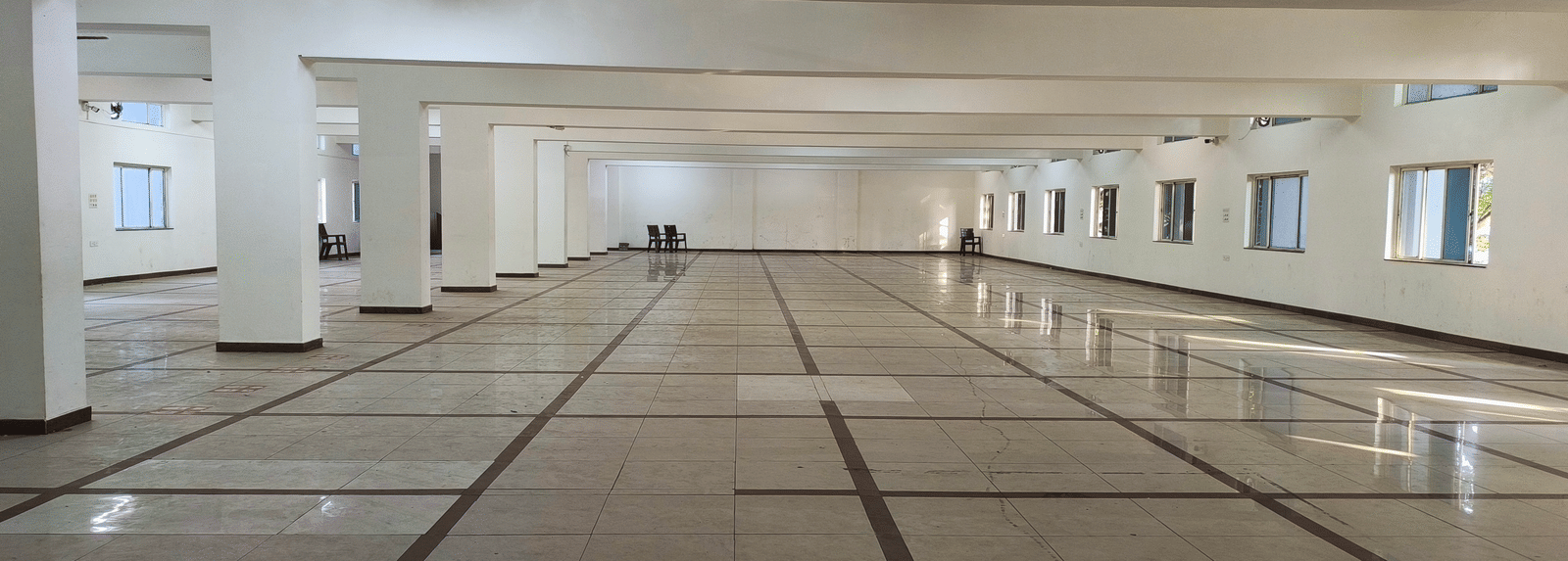 A wide shot of a large, empty banquet hall in BNGV Grandeur Hotel and Banquets, emphasising the hall's length and polished surfaces.