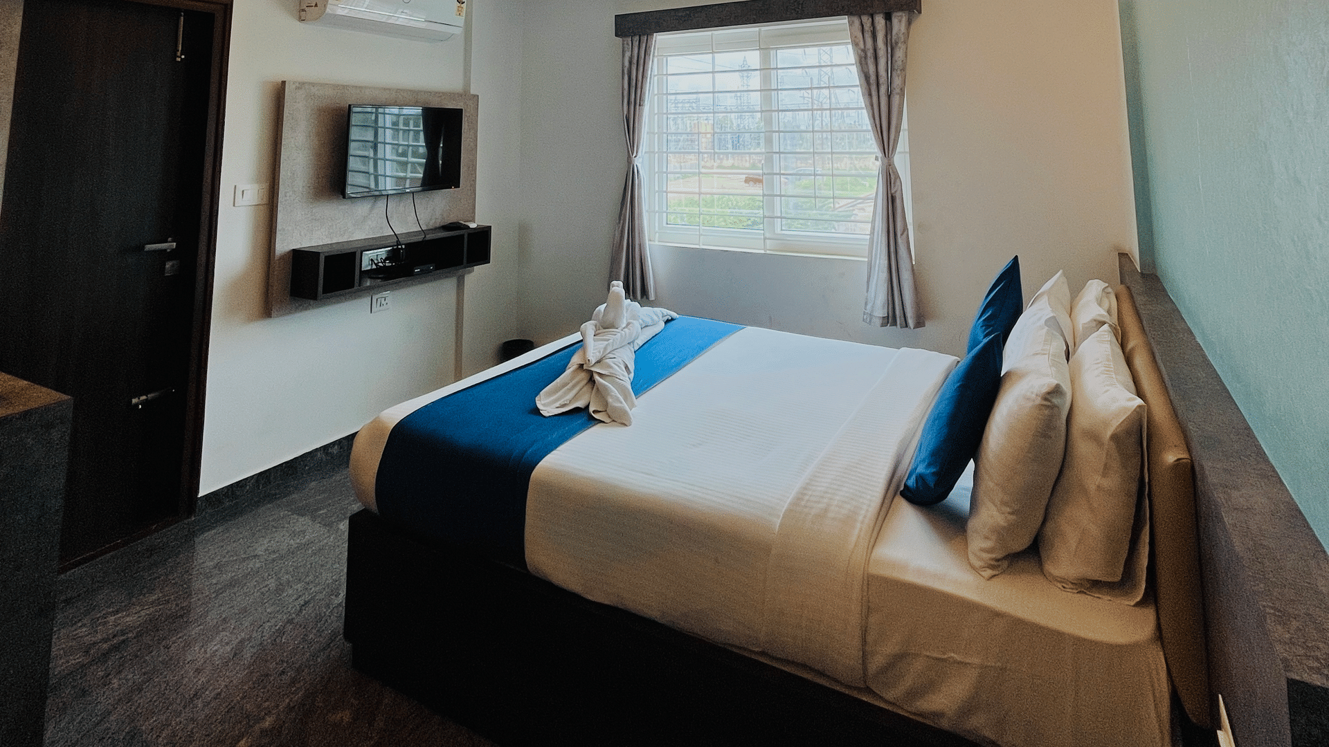 Queen bed under a recessed ceiling with warm cove lighting and a wall mounted TV in the Standard Balcony Room at Value Inn, Bangalore Airport