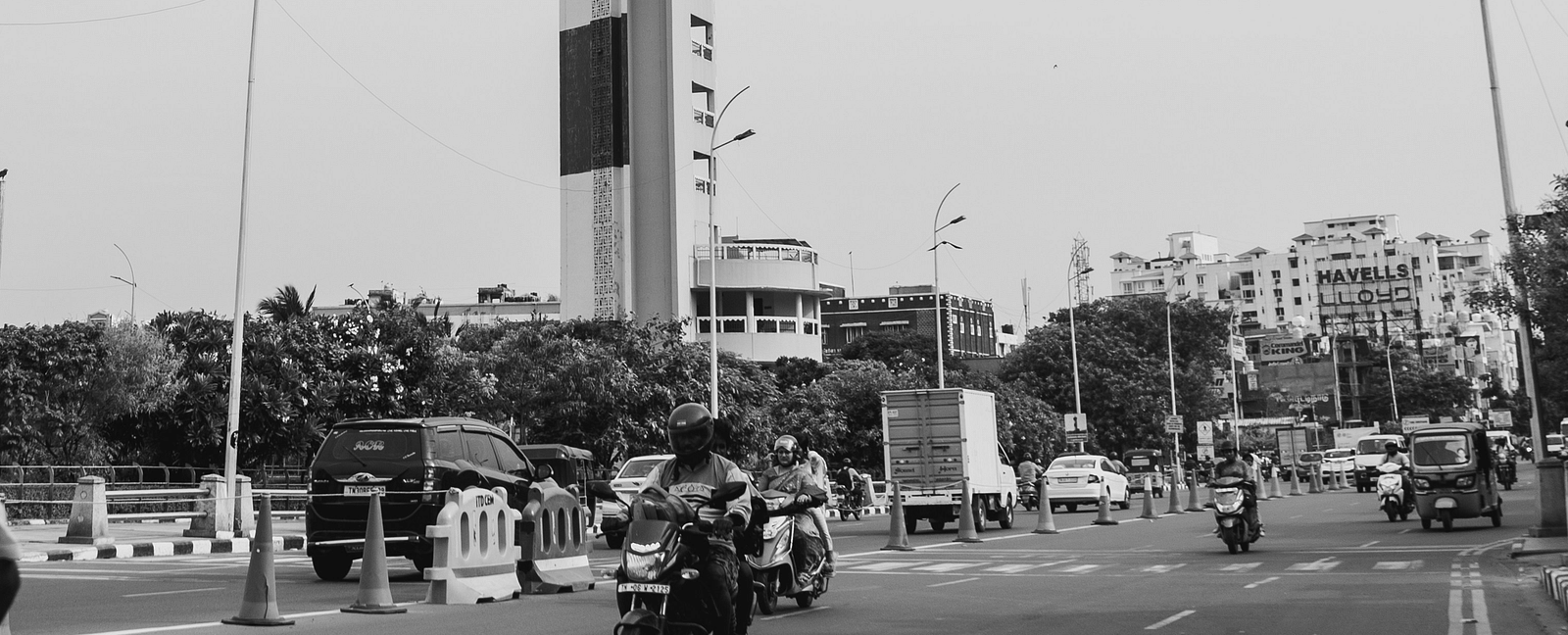 An overview of a light house in Chennai with bikes riding on the road next to it.