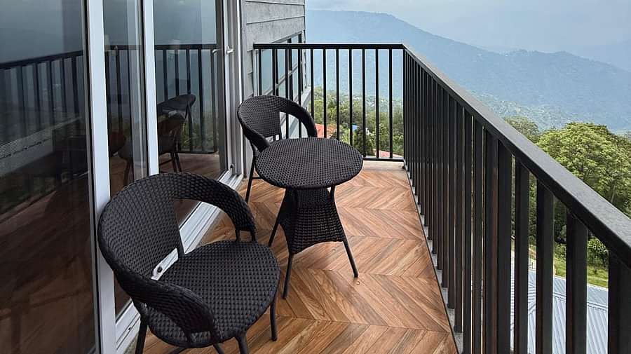 A modern balcony at Summit Enigma Resort & Spa, with black metal railings and herringbone-patterned flooring, offers a scenic view of distant mountains under a cloudy sky.   Sources