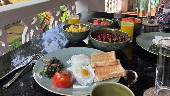 An image of a breakfast table where several dishes are placed like omelette, bread, curries, bowl of fruits, a glass of cold drink and lot more at Lamrin Ucassaim Hotel, Goa