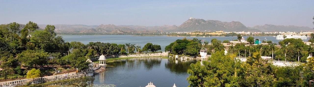 Serene view of Lake Pichola with lush greenery under the blue sky with the backdrop of the hills. Having a Udaipur Guide will make your trip exponentially better.