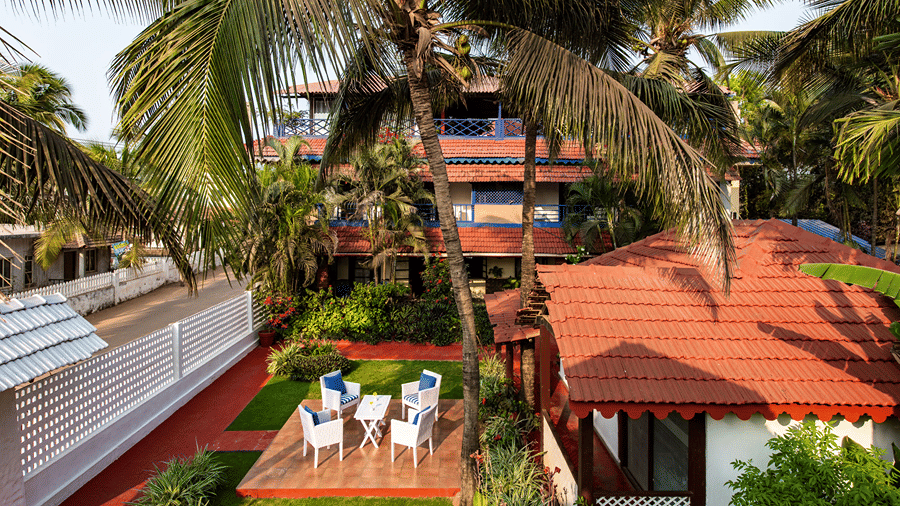Elevated view of red-roofed cottages, palm trees, garden seating and a swimming pool.