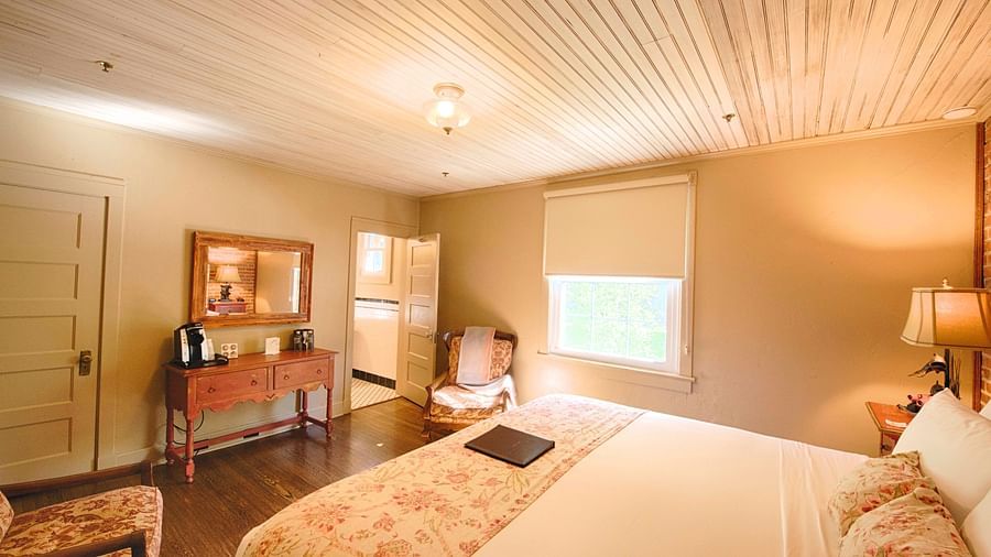 side view image of a bedroom highlighting the smooth sheets spread over the double bed along with a wooden table opposite to it - Historic Tapoco Lodge 