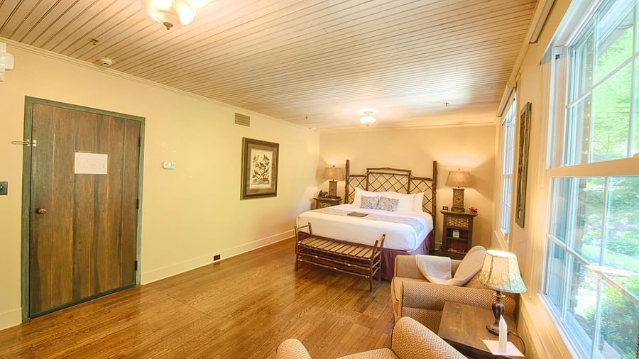 dull view image of a bedroom with a wooden door featuring a plush double bed with two bed side tables on either side of it - Historic Tapoco Lodge