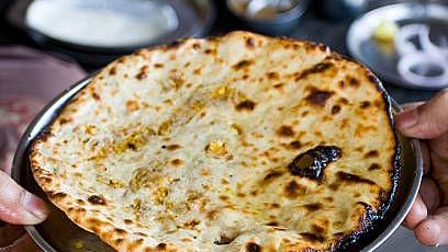 A close-up of a freshly cooked stuffed naan or paratha on a plate.