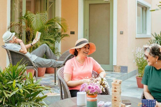 Three people sitting on a patio outside a peach coloured building, engaged in conversation at Karma Chalets.