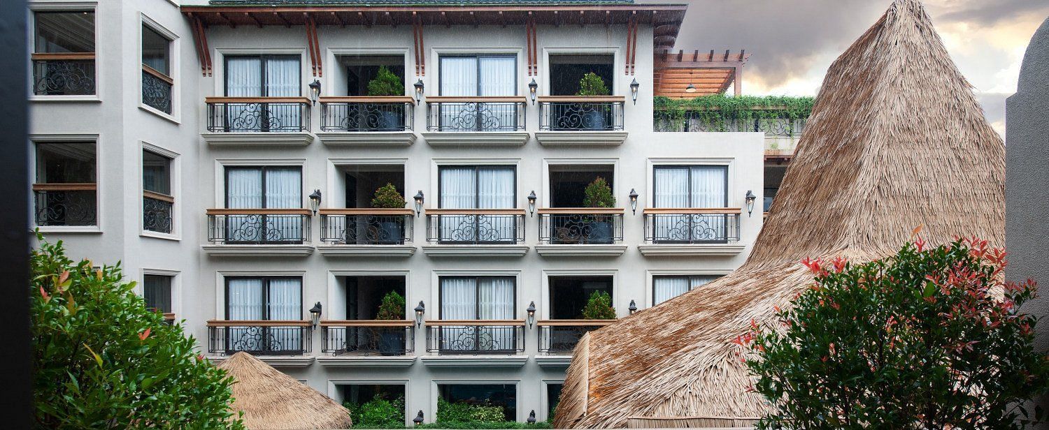 An exterior view of the multi-story hotel building at The Evren, Vagator, with a view of balconies and the swimming pool below. The image shows the building's architecture and the surrounding tropical environment under a dramatic sky.