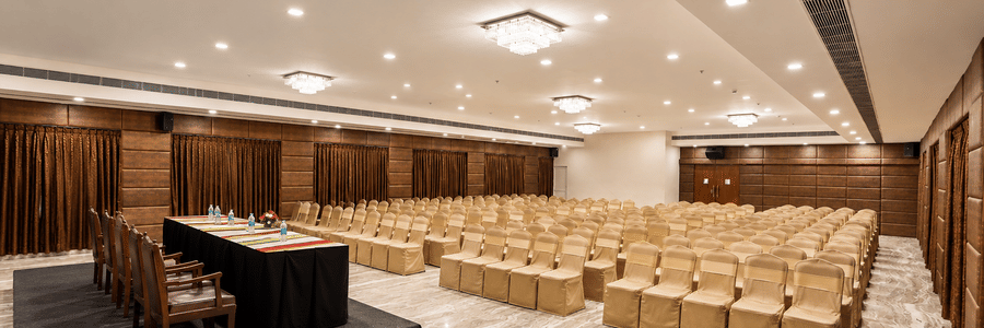 A hall with multiple chairs, chandeliers, and a stage at Raj Park, Chennai.