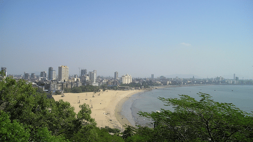 An aerial view of Mumbai's sky line in the distance with the Arabian Sea and a beach in view.