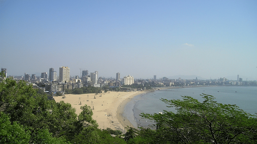 An aerial view of Mumbai's sky line in the distance with the Arabian Sea and a beach in view.