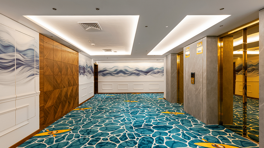 The corridors feature white and wooden-finished walls, with blue wave designs in the centre, and the carpeted floor displays a playful water pattern at Cloud9 Sarovar Premiere, Palolem Goa