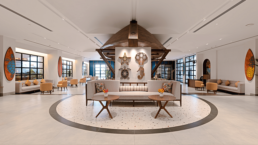 A lounge area features a spacious sofa and a three-legged wooden table with a vase of flowers in the centre. The wall is adorned with sea-themed, wall-mounted decorations at Cloud9 Sarovar Premiere, Palolem Goa