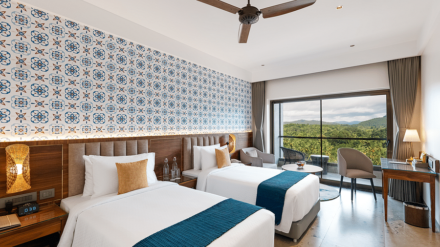 The view of twin beds, side tables, and a work desk with a chair in one of the rooms at Cloud9 Sarovar Premiere, Palolem Goa, offers a comfortable and functional space
