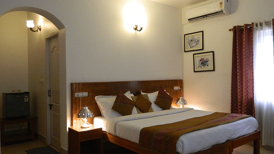 Image of Premium AC Cottage at Fantasy Golf Resort Bangalore in warm lighting featuring a double bed placed next to the window and a lamp next to the nightstand