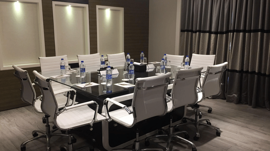 Sleek boardroom with a dark glass table, white office chairs, and water bottles arranged for a meeting.