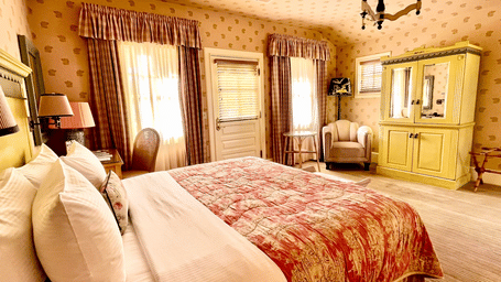 Side view of a rom at Tallman Hotel having double bed facing patterned wall and vintage furniture