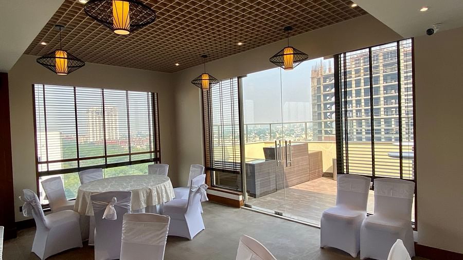 An image of a banquet hall with its seating arrangement, subtle decoration with lighting and an expansive glass door leading outdoor - Hideaway banquets & Lawns, Greater Noida