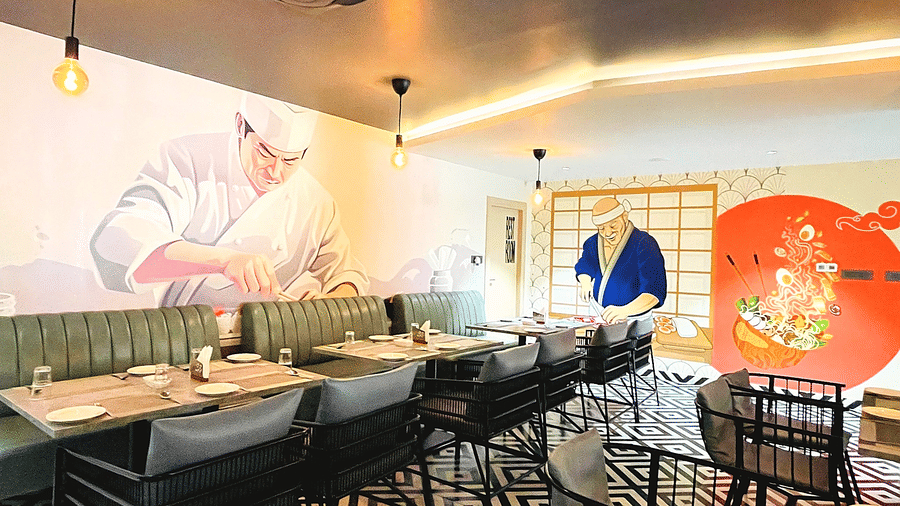 A restaurant dining area at Hotel Kyzen HiTech City featuring green upholstered seating patterned floor tiles pendant lighting and a large floral mural artwork on the white wall.