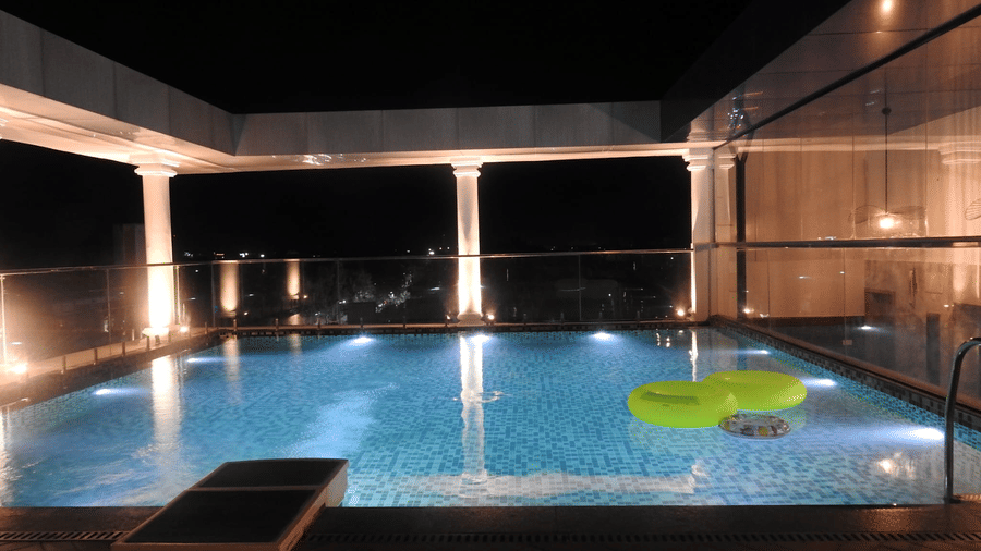 A rooftop swimming pool at Sands Point Hotel, Pondicherry, featuring 2 inflatable green floating rings in a tiled pool with underwater lights.