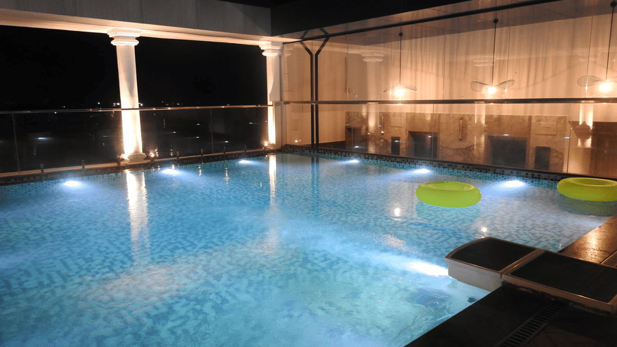 A rooftop swimming pool at Sands Point Hotel, Pondicherry with underwater lights in a tiled pool, 2 green inflatable rings floating on the water.