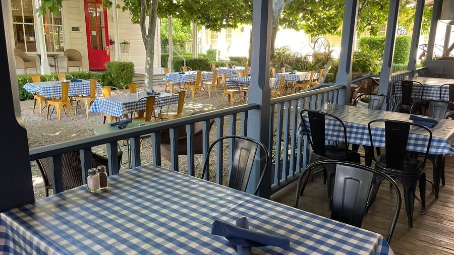 A view of Tallman Hotel representing a Dining setup on a deck with checkered table cloths with a view of outdoor dining seating.