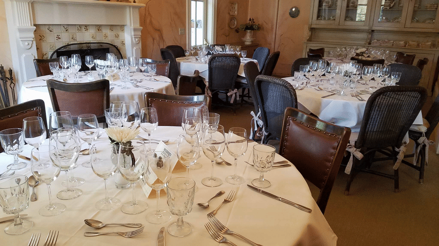 An elegant dining area at Tallman Hotel featuring table linens, cushioned armchairs, a fireplace mantel, and rustic wooden interiors with ambient lighting.