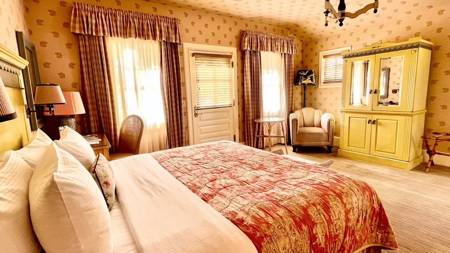 Side view of a rom at Tallman Hotel having double bed facing patterned wall and vintage furniture