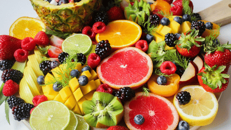 A close-up, overhead photo of a brightly coloured wooden board overflowing with sliced citrus, kiwi, mango, pineapple, and berries.