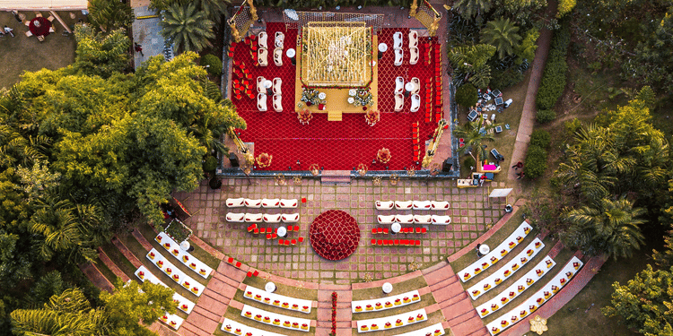Aerial view of an outdoor wedding venue with neatly arranged white chairs and a floral-decorated altar, surrounded by lush greenery