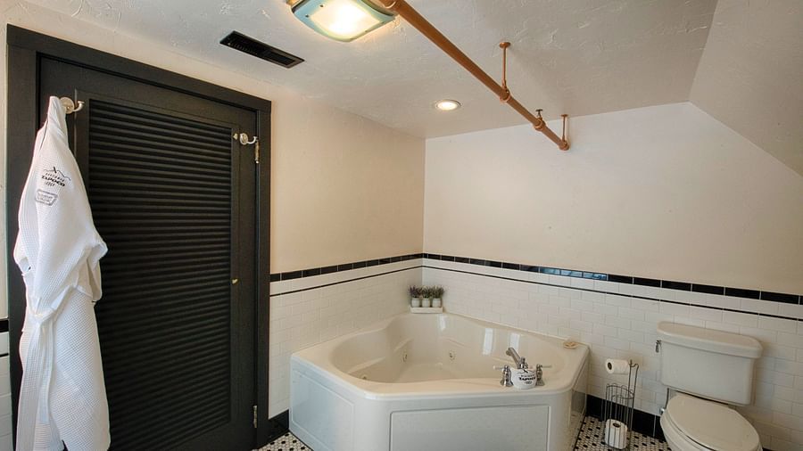 a luxurious bathroom featuring a full size bathtub beside a huge black door with a bathrobe hanging over it - Historic Tapoco Lodge