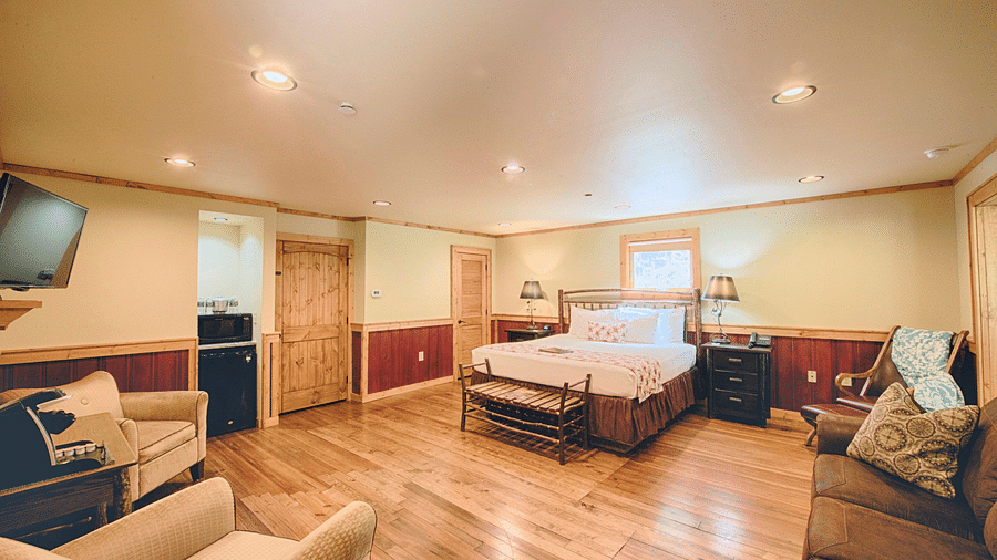 corner view image of a bedroom featuring a plush double bed in the middle and a seating area opposite to it - Historic Tapoco Lodge
