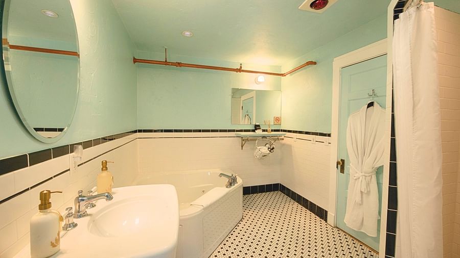 full view image of the bathroom with a wash basin along with a bathtub and a bathrobe hanging behind the door of the bathroom - Historic Tapoco Lodge