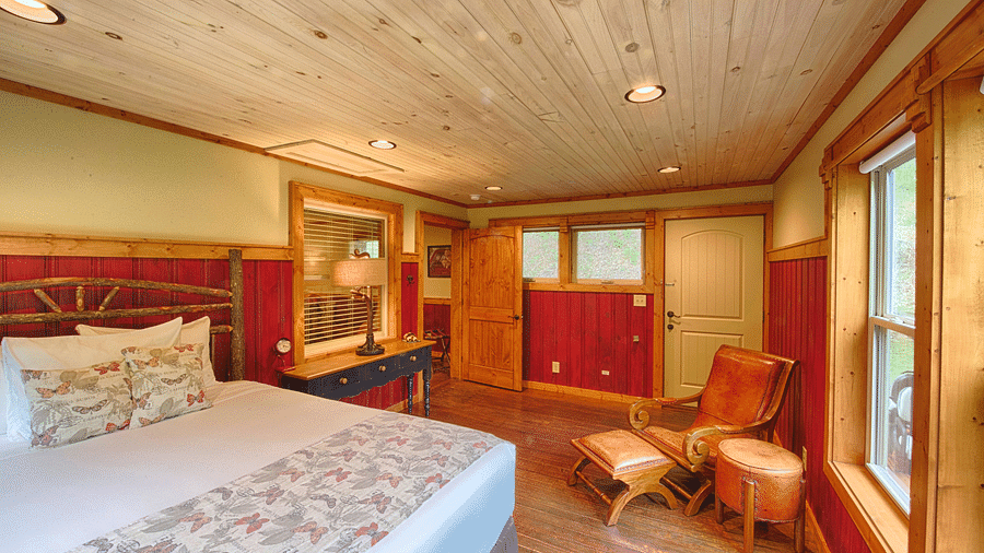 a bedroom with an armchair in the corner and a double bed along with an open door in the far end of the room - Historic Tapoco Lodge