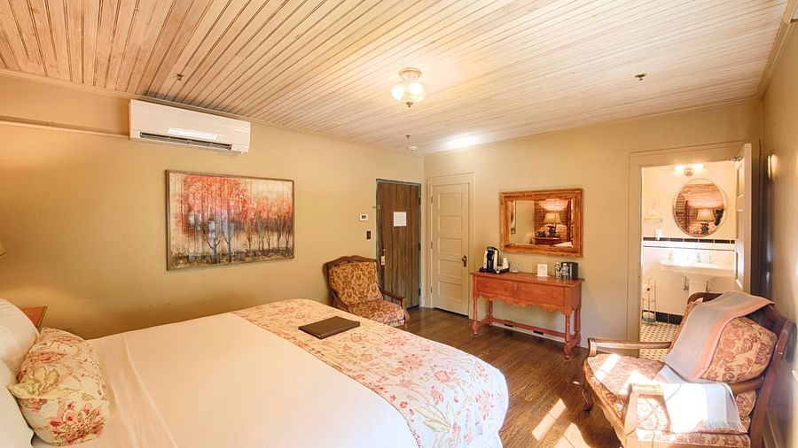 corner view image of a bedroom with two armchairs facing towards each other in front of the bed along with a wall mounted air-conditioner - Historic Tapoco Lodge