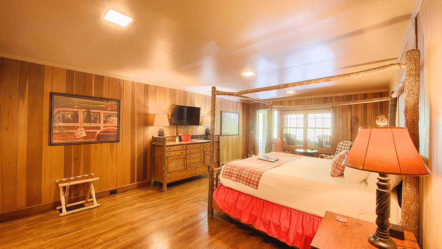 a double bed with a lamp kept on side table placed opposite to a wall mounted television in a room with wooden interiors - Historic Tapoco Lodge