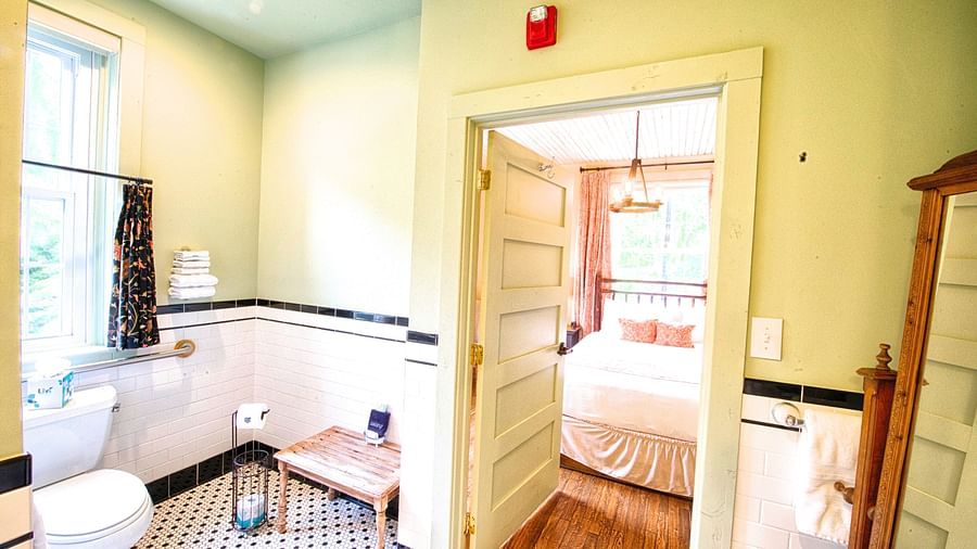 a brightly lit bathroom with a commode and rack in the corner featuring a door opening to the bedroom - Historic Tapoco Lodge