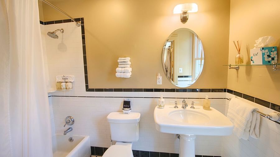 a bathroom highlighting a wash basin with an oval shaped mirror along with a commode and a bathtub besides it - Historic Tapoco Lodge