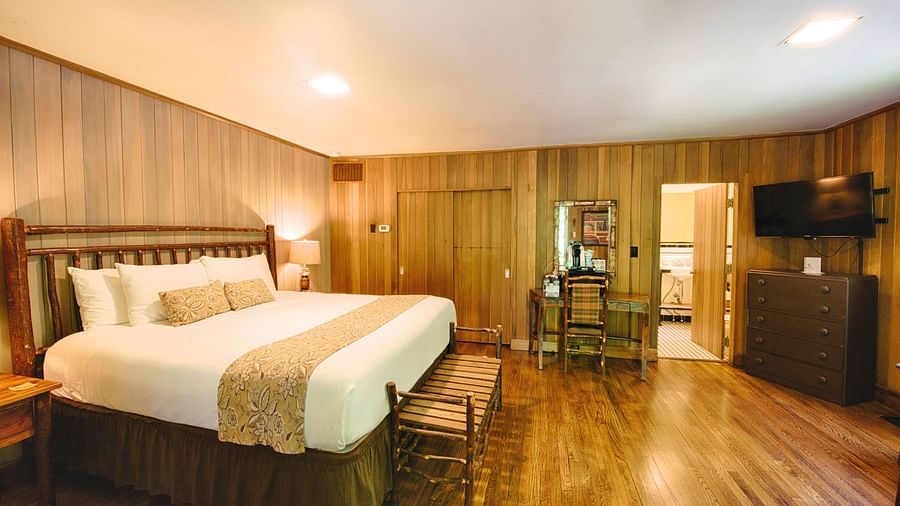 corner view image of a cozy bedroom with a double bed and wooden interiors along with a wall mounted television in the corner - Historic Tapoco Lodge